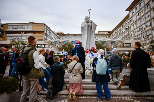 Biskop og troende ber rosenkransen foran Johannes Paul II-statuen utenfor Gemelli-sykehuset i Roma