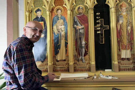 En mann sitter foran helgenbildene av St. Hallvard og St. Magnus i St. Olav domkirke i Oslo