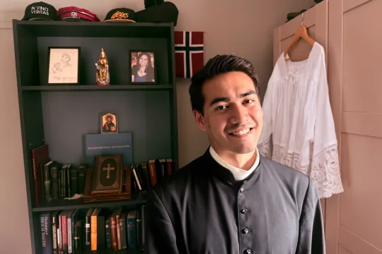 Diakon Mathias Ledum foran bokhyllen sin