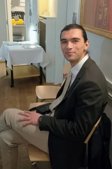 En ung mann sitter på en stol i menighetssalen i Akersveien og smiler mot kamera 