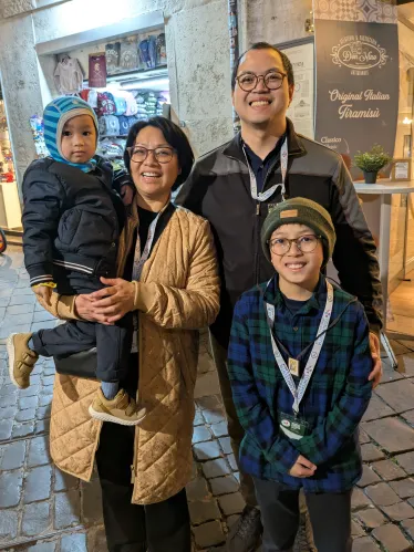 En familie med mor, far og to barn står på en gate i Roma og smiler til kamera