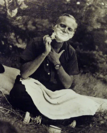 En ung Karol Wojtyla, kledd uformelt, sitter på gresset og barberer seg