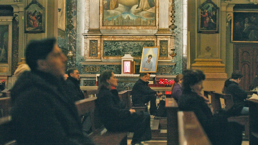 Mennesker sitter i en kirke med et bilde av Carlo Acutis på alteret