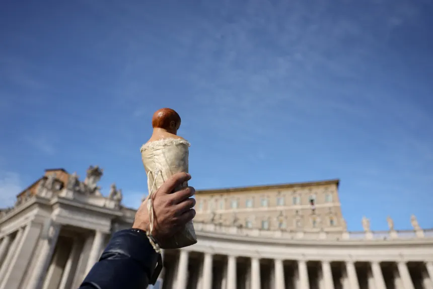 En person holder opp en figur av Jesusbarnet på Petersplassen i Vatikanet