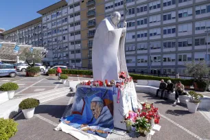 Et stort bilde av pave Frans ligger mot sokkelen av Johannes Paul II-statuen utenfor Gemelli-sykehuset