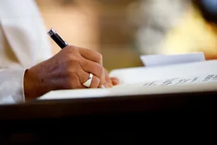 Nærbilde av hånden til pave Frans som signerer et dokument med en penn