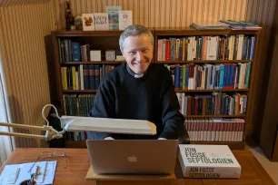 En prest sitter foran en laptop ved skrivebordet på kontoret sitt